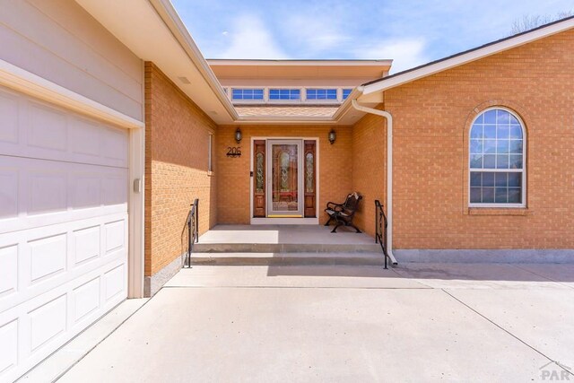 property entrance with brick siding, driveway, and an attached garage