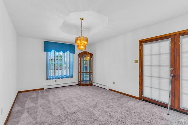 unfurnished room featuring a tray ceiling, an inviting chandelier, a baseboard heating unit, light carpet, and baseboards