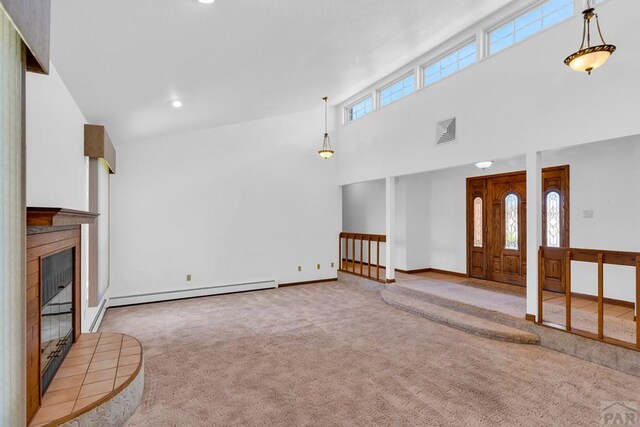 unfurnished living room with a baseboard radiator, light colored carpet, visible vents, a towering ceiling, and a tiled fireplace