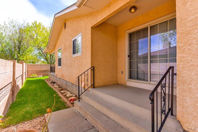 view of exterior entry with a yard, fence, and stucco siding