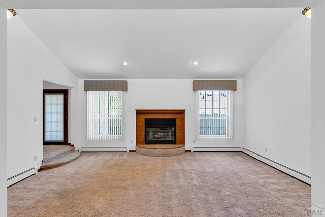 unfurnished living room featuring lofted ceiling, a baseboard radiator, light carpet, and a wealth of natural light