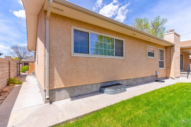 view of home's exterior with stucco siding, a lawn, a gate, a patio area, and fence