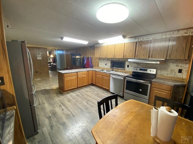 kitchen with brown cabinets, light countertops, light wood-style flooring, appliances with stainless steel finishes, and a peninsula