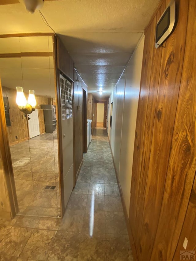 corridor featuring a textured ceiling and wood walls