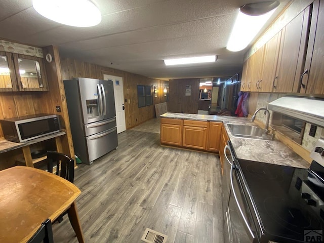 kitchen with a peninsula, a sink, light countertops, appliances with stainless steel finishes, and brown cabinetry