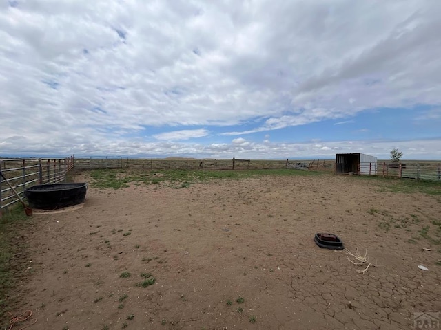 view of yard featuring an outbuilding, an exterior structure, an enclosed area, fence, and a rural view