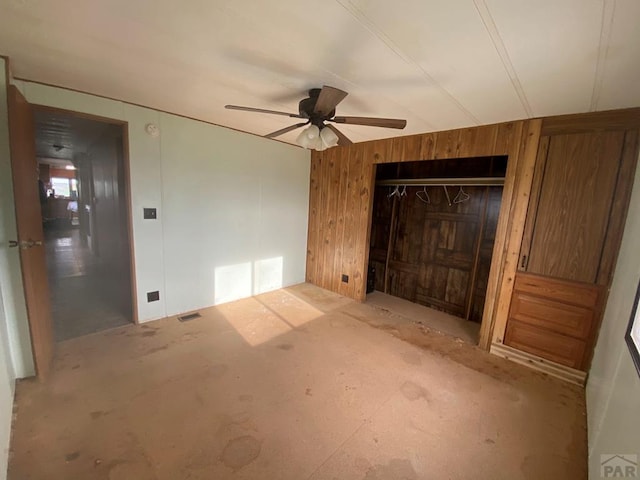 unfurnished bedroom with a closet, ceiling fan, and wooden walls