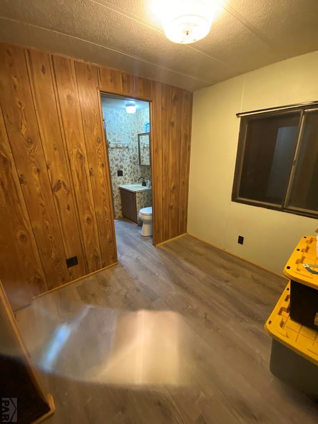 interior space featuring a sink, wooden walls, a textured ceiling, and wood finished floors