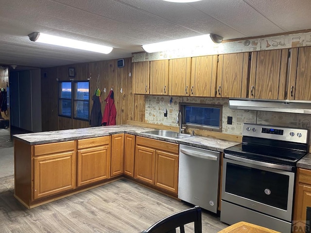 kitchen with under cabinet range hood, stainless steel appliances, a peninsula, a sink, and light wood-style floors