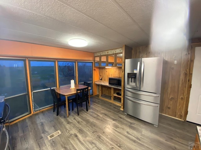 kitchen with visible vents, brown cabinetry, wood finished floors, black microwave, and stainless steel refrigerator with ice dispenser