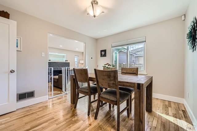 dining space with baseboards, visible vents, a tiled fireplace, and light wood finished floors