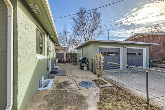 view of side of home featuring a detached garage, fence, an outdoor structure, and stucco siding