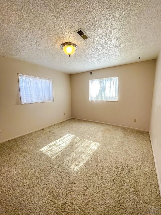 empty room featuring a textured ceiling, carpet, visible vents, and baseboards