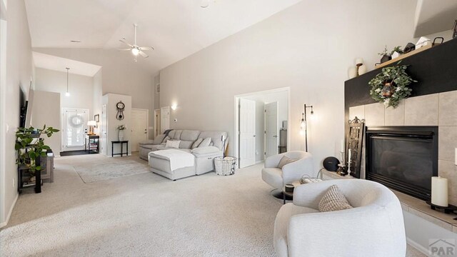 living area with ceiling fan, high vaulted ceiling, carpet flooring, and a tile fireplace