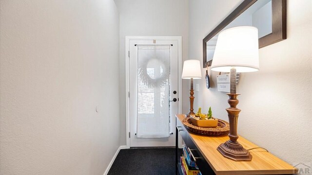 doorway to outside featuring dark colored carpet and baseboards