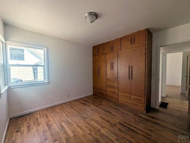 unfurnished bedroom with baseboards, a closet, visible vents, and wood finished floors