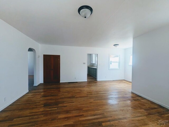 unfurnished room featuring arched walkways, dark wood-style flooring, and baseboards