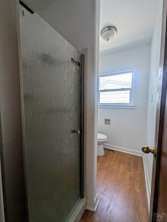 full bathroom with toilet, a shower stall, baseboards, and wood finished floors