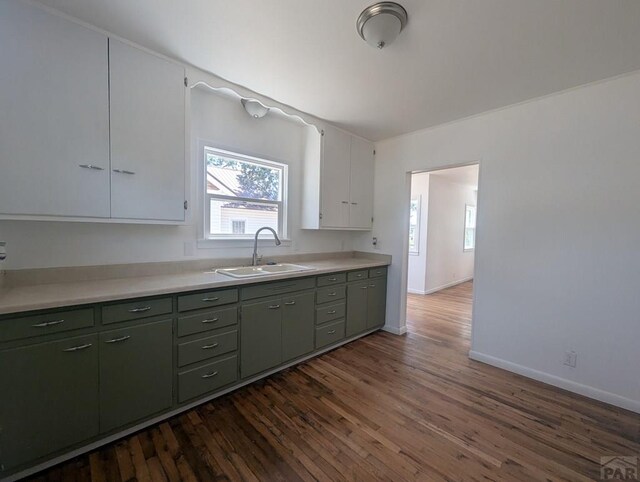 kitchen with dark wood-type flooring, a sink, white cabinetry, baseboards, and light countertops