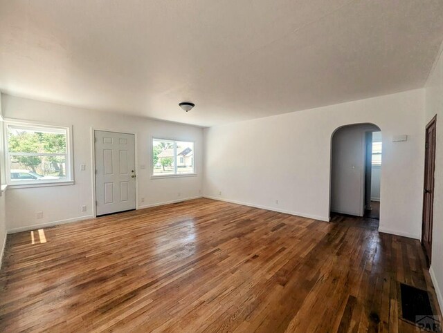 empty room featuring dark wood-style floors, arched walkways, and baseboards