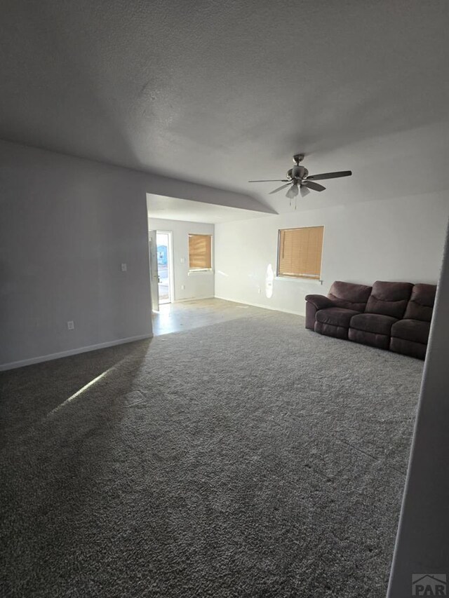 unfurnished living room featuring a ceiling fan, dark carpet, a textured ceiling, and baseboards