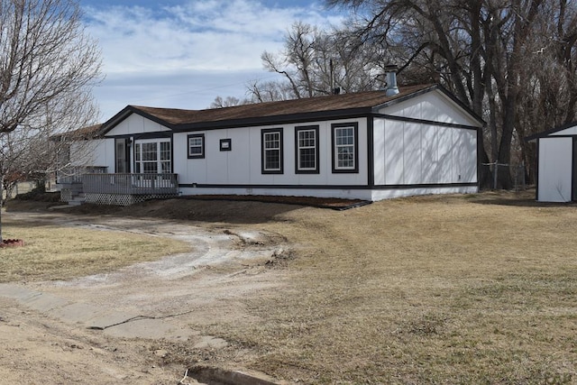 view of front of home featuring a front yard, dirt driveway, a deck, and an outdoor structure