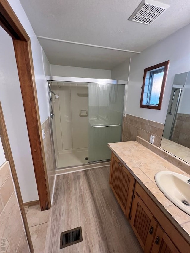 full bath with vanity, wood finished floors, a shower stall, and visible vents