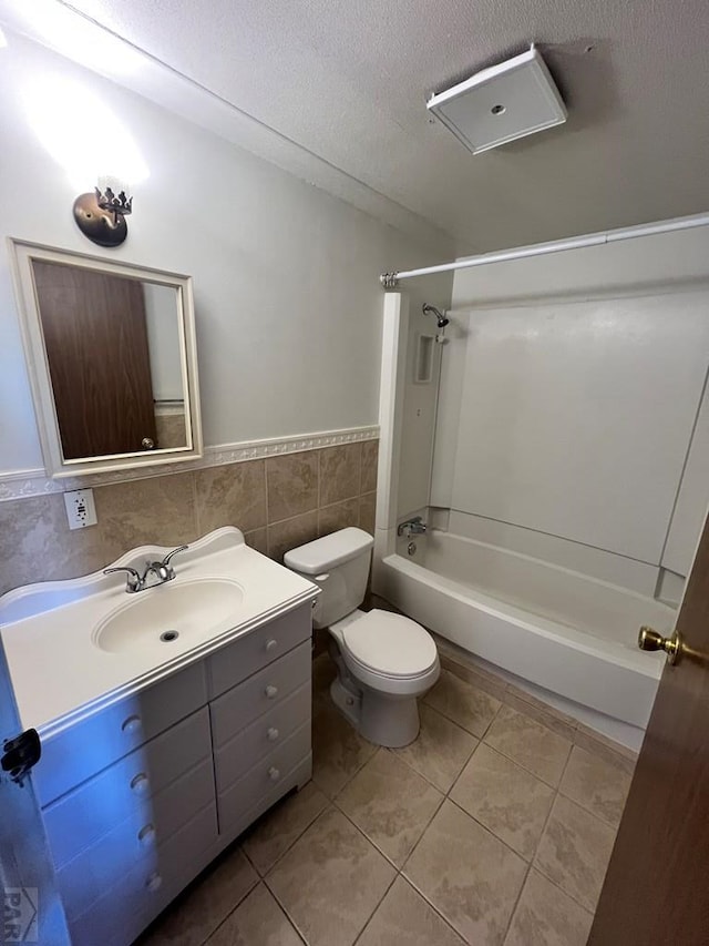 bathroom with a textured ceiling, tile patterned flooring, vanity, tile walls, and washtub / shower combination