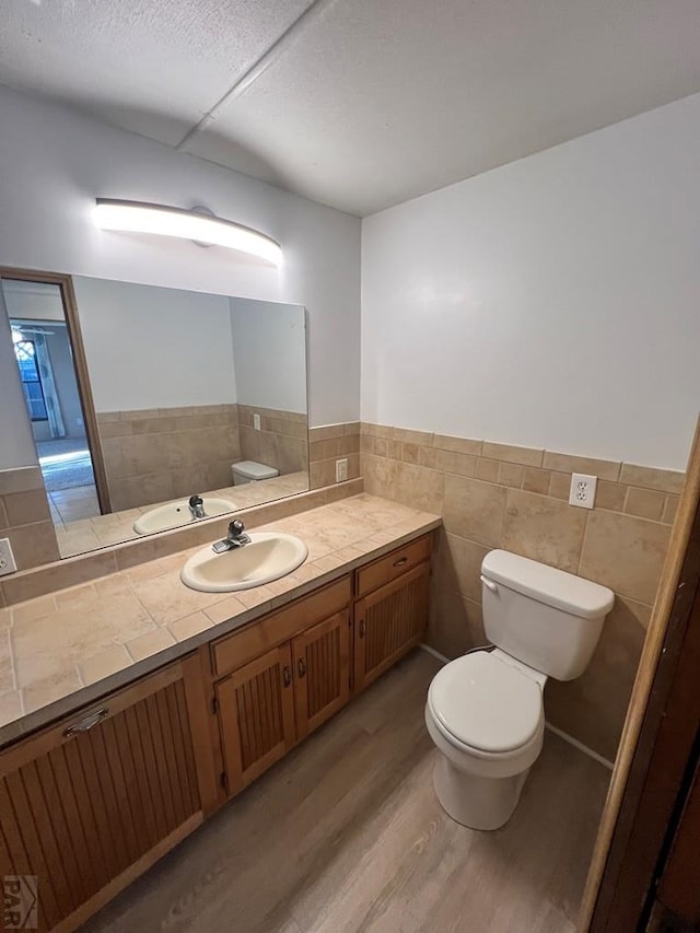 bathroom featuring a wainscoted wall, tile walls, toilet, vanity, and wood finished floors