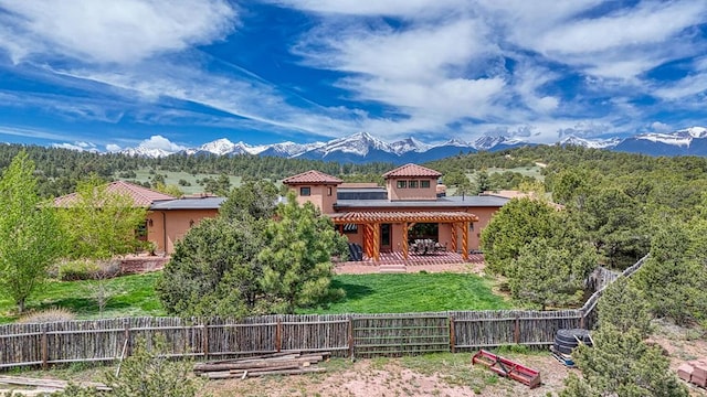 view of front of property featuring a patio, a fenced backyard, a tiled roof, a mountain view, and stucco siding