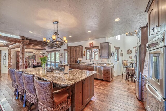 kitchen featuring a kitchen island, appliances with stainless steel finishes, light stone countertops, light wood-style floors, and pendant lighting