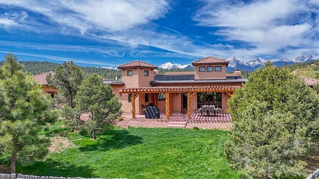 rear view of house with a mountain view, a tiled roof, a lawn, stucco siding, and a patio area