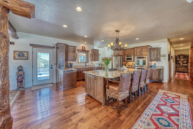 kitchen with brown cabinetry, a large island, appliances with stainless steel finishes, dark wood-type flooring, and pendant lighting