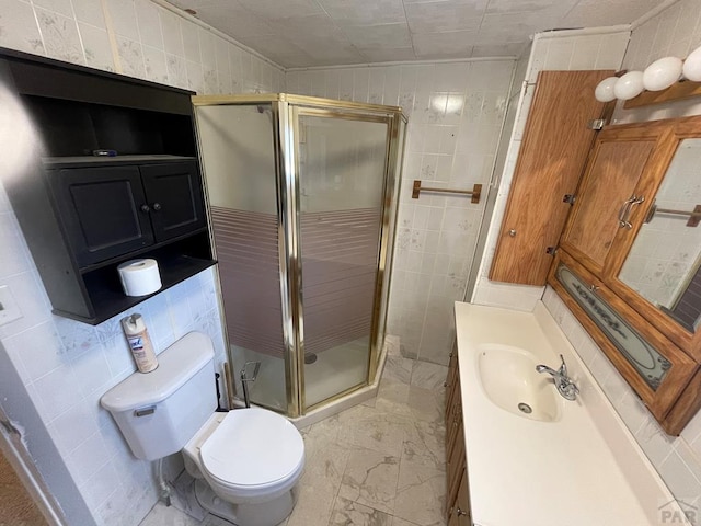 bathroom featuring toilet, marble finish floor, vanity, a shower stall, and tile walls