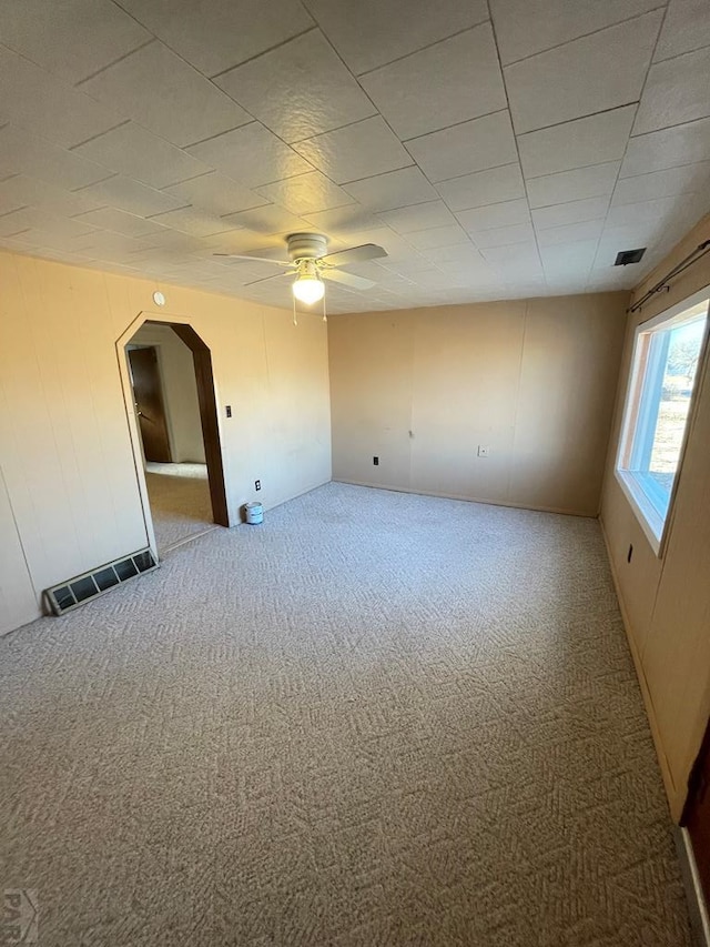 carpeted empty room with a ceiling fan, arched walkways, and visible vents