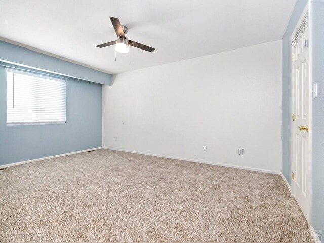 spare room featuring a ceiling fan, light carpet, and baseboards