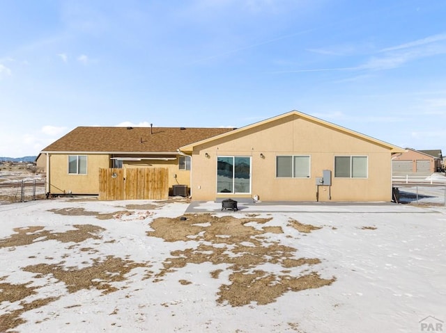 snow covered house featuring stucco siding, fence, and central AC unit