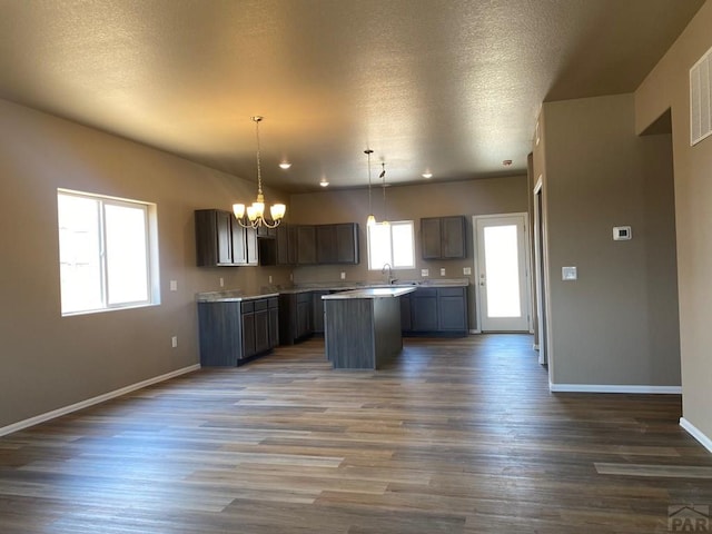 kitchen with a notable chandelier, dark wood-type flooring, light countertops, a center island, and pendant lighting