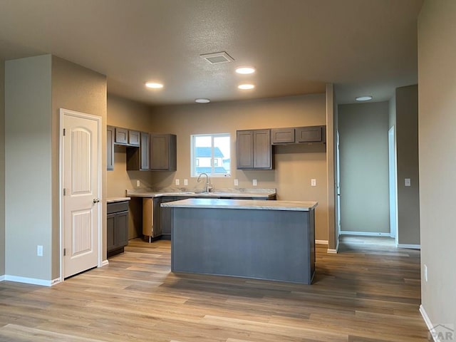 kitchen with a center island, light countertops, visible vents, light wood-type flooring, and baseboards