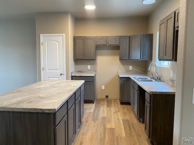 kitchen with light countertops, light wood finished floors, a sink, and a center island