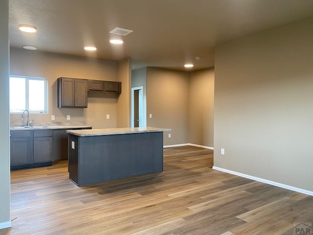 kitchen with light wood-type flooring, light countertops, a sink, and baseboards