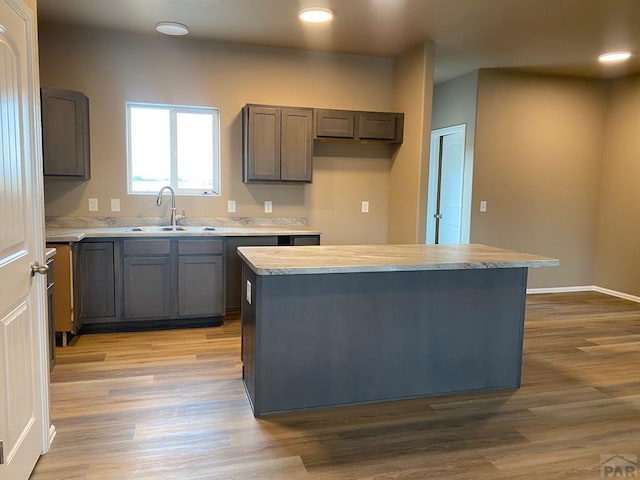 kitchen with light wood-type flooring, light countertops, a sink, and a center island