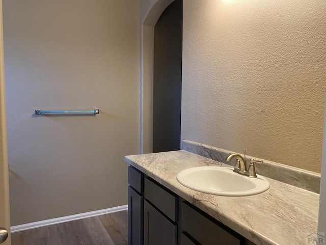 bathroom featuring a textured wall, vanity, baseboards, and wood finished floors