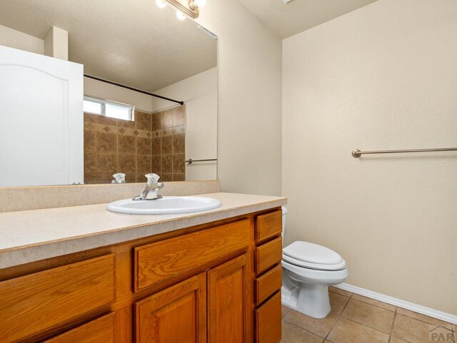 bathroom with a shower, toilet, vanity, tile patterned flooring, and baseboards