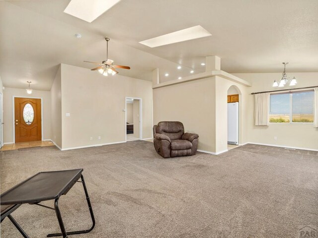 carpeted living room with vaulted ceiling with skylight, a healthy amount of sunlight, arched walkways, and baseboards