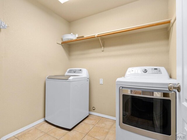 washroom with light tile patterned floors, laundry area, separate washer and dryer, and baseboards