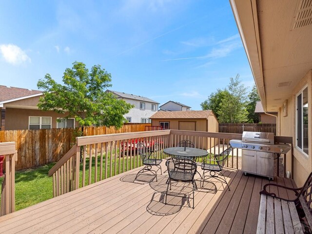 wooden deck with an outbuilding, outdoor dining space, grilling area, and a fenced backyard