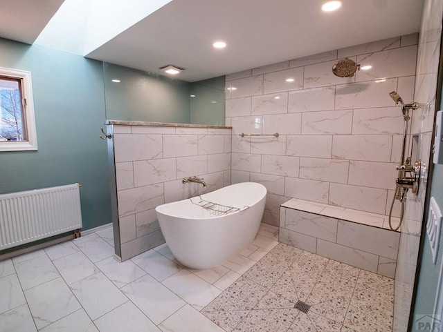 full bathroom with marble finish floor, tile walls, radiator heating unit, a walk in shower, and a freestanding tub