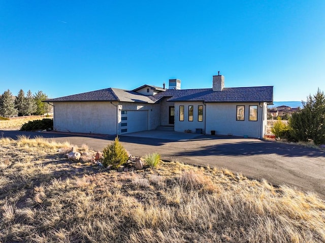 view of front of home with a garage, concrete driveway, a chimney, and stucco siding