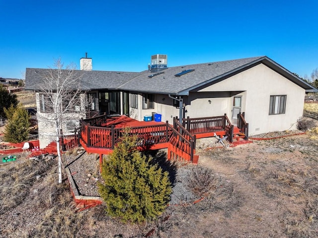 rear view of house featuring a chimney, central air condition unit, a shingled roof, stucco siding, and a wooden deck